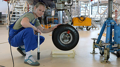 Eine junge Frau beim Radwechsel am Flugzeug.