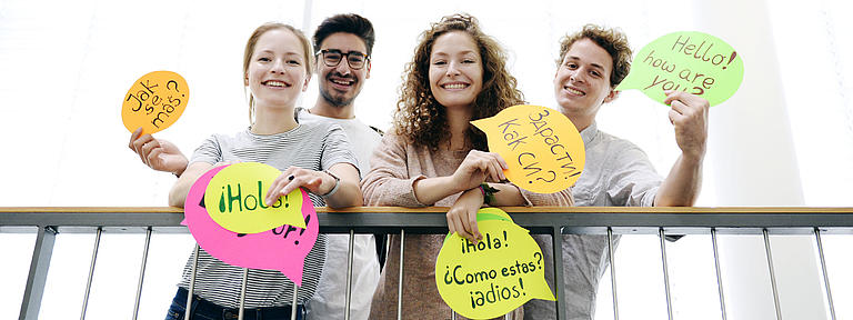Four young people are showing colourful cards with greetings in different languages on them.