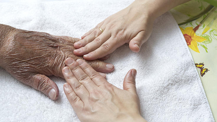 Junge Hände streichen über die Hand einer älteren Person