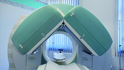 In einem medizinischen Behandlungsraum einer Radiologie steht ein Kernspintomographiegerät. Im Vordergrund ist die  Liegefläche für Patienten zusehen.