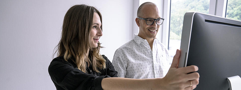 Eine Frau und eine Mann mit Brille schauen auf einen Computerbildschirm