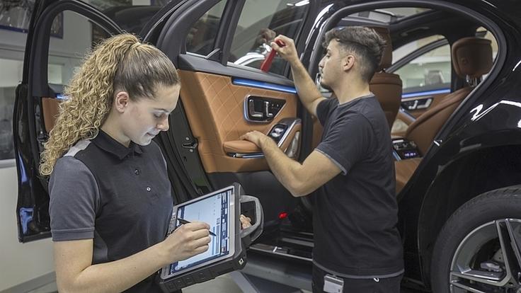 Zwei Auszubildende arbeiten mit Tablet und Werkzeug an einem Auto.