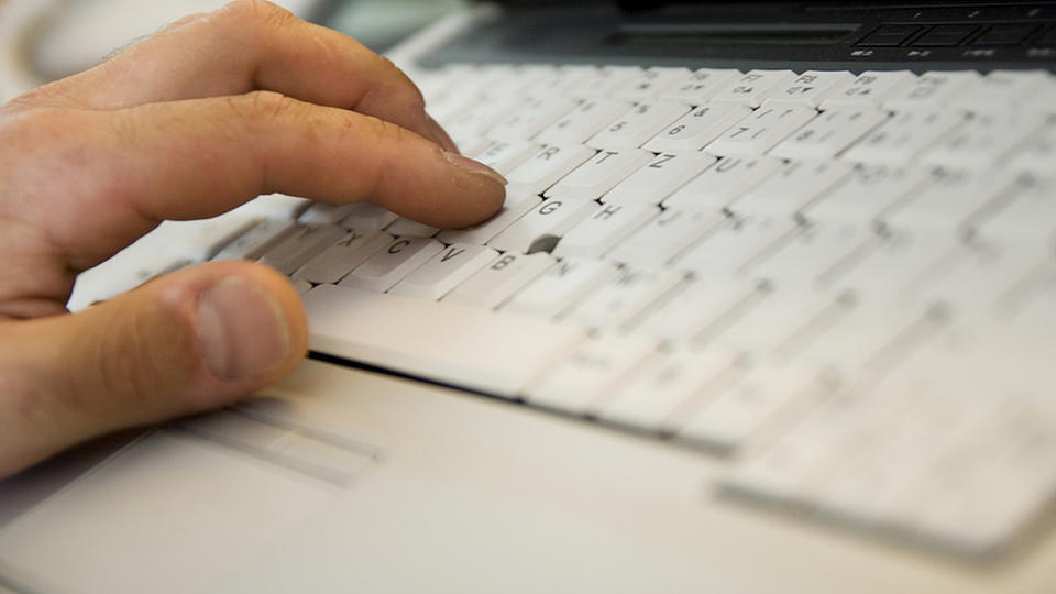 Nahaufnahme der Tastatur von einem Laptop, auf der Tastatur ruht die linke Hand einer Person.