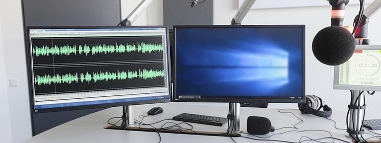 Zwei Computerbildschirme und Mikrofone in einem Aufnahmestudio