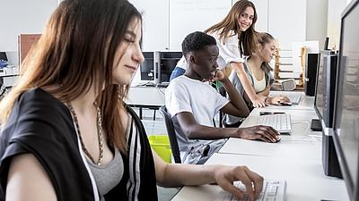 Schülerinnen und Schüler testen Check-U zusammen mit einer Lehrerin an Computern.