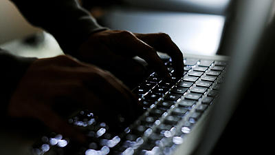Zwei Hände tippen in dunkler Umgebung auf einer schwarzen Tastatur.
