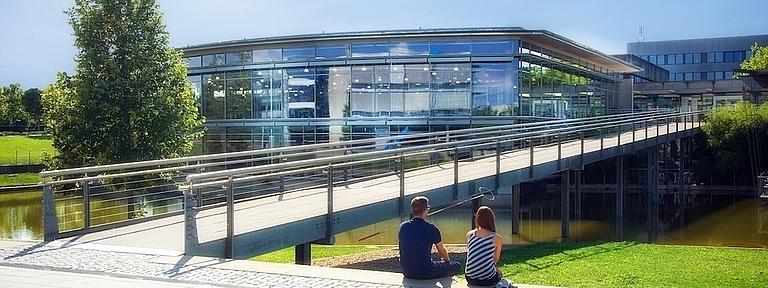 Zwei Personen sitzen neben einer Brücke auf dem Campus der Hochschule Regensburg.