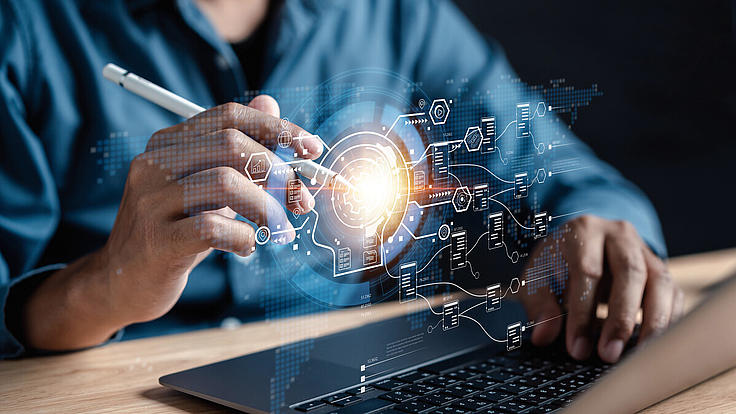 Person am Laptop aktiviert mit einem elektronischen Stift holografische Symbole über der Tastatur. 