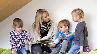Eine Frau liest mit drei Kindern ein Buch.