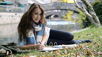 Eine Studentin liegt auf einer Wiese und lernt.