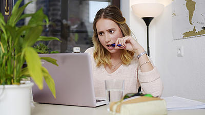Eine junge Frau schaut in einen Laptop und kaut auf einem Stift.