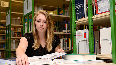 Eine Studierende sitzt in einer Bibliothek.