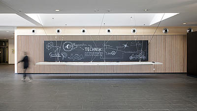 A slate with inscriptions hangs in the foyer of a modern building.