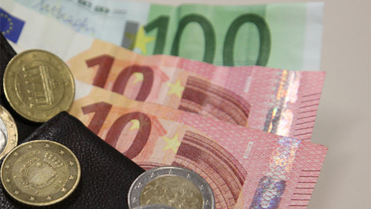 Unter einer schwarzen GeldbÃ¶rse liegen ein Einhundert-Euro-Schein sowie zwei Zehn-Euro-Scheine. Auf der Geldbörse liegen fünf Geldstücke.