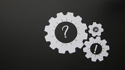Auf schwarzem Grund sind drei weiße, ineinander greifende Zahnräder abgebildet. Auf zwei Zahnrädern befindet sich jeweils ein Fragezeichen, am dritten ein Ausrufezeichen.