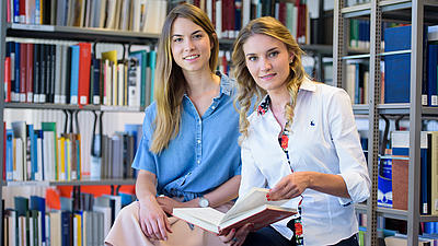 Studierende suchen in der Bibliothek nach passenden Büchern