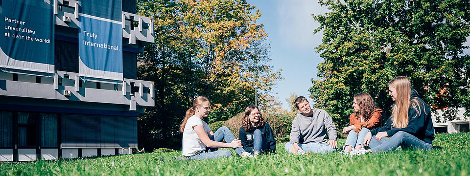 Studierende sitzend auf einer grünen Wiese vor der Hochschule