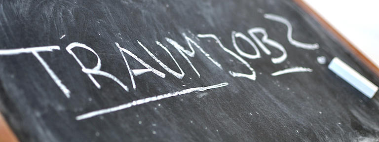 Auf einer schräg liegenden Schreibtafel mit Holzrand steht in Großbuchstaben das Wort "Traumjob"