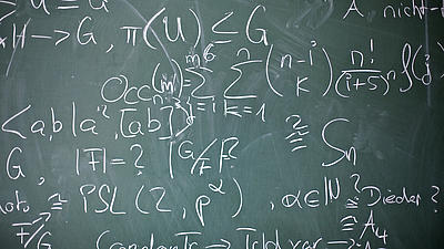 Auf einer dunkelgrünen Tafel wurden mit weißer Kreide verschiedene Formeln aufgeschrieben und Berechnungen angestellt.