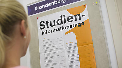 Eine junge Frau schaut sich ein Plakat zu einem Studieninformationstag an.