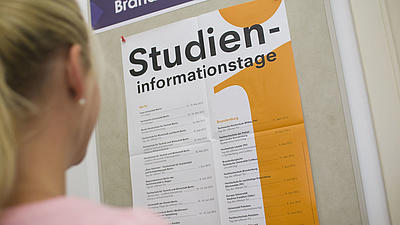 Eine junge Frau schaut sich ein Plakat zu einem Studieninformationstag an.