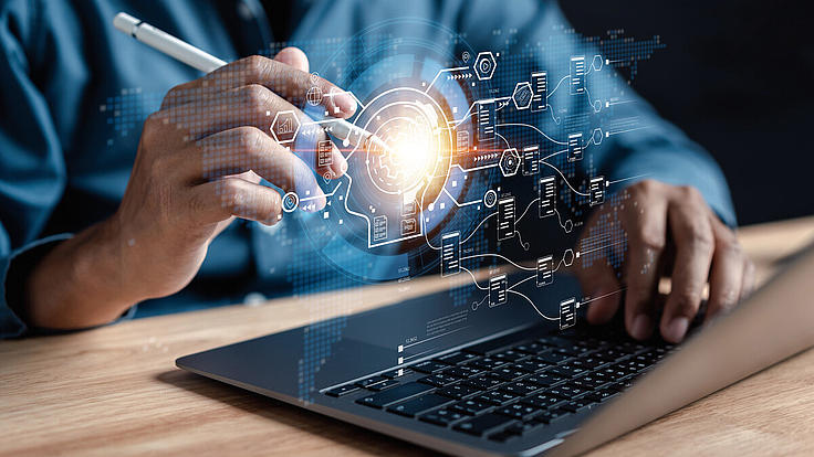 Person am Laptop aktiviert mit einem elektronischen Stift holografische Symbole über der Tastatur. 