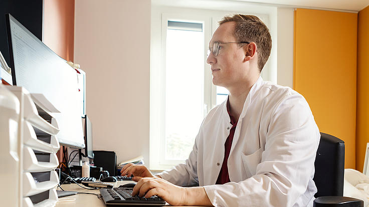 Erik K. sitzt vor einem Rechner und bearbeitet digitale Patientenakten.