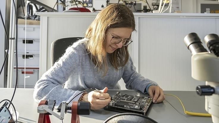 Eine junge Frau untersucht eine elektronische Leiterplatte.