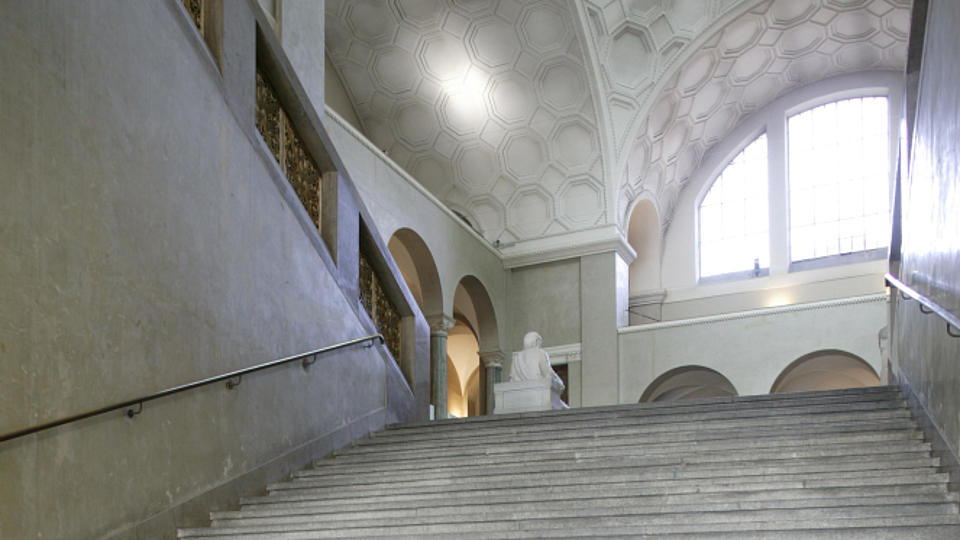 Zu sehen ist ein ehrwürdiges, marmornes Treppenhaus in einer Universität.