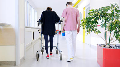 Junger Krankenpfleger hilft einer Patientin mit einer Gehhilfe bei Wiedererlernen des Gehens.