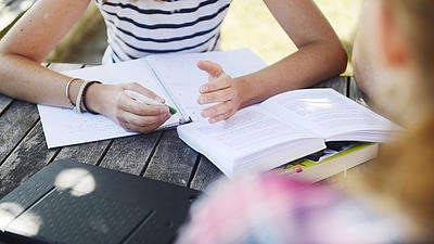 Zwei Frauen sitzen an einer Bank und bereiten sich mit Büchern auf eine Prüfung vor