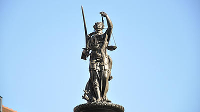 Aufgenommen aus der Froschperspektive sieht man eine Statue der Göttin der Gerechtigkeit, Justitia vor blauem Himmel.