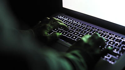Nahaufnahme von zwei Händen einer dunkel gekleideten Person, die auf der Tastatur eines Laptops ruhen.