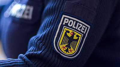 Nahaufnahme eines Polizeiwappens auf einem blauen Pullover am linken Oberarm einer Polizistin.