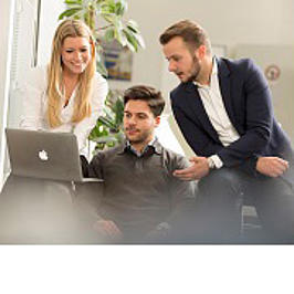 Drei Studierende schauen in einen Laptop.