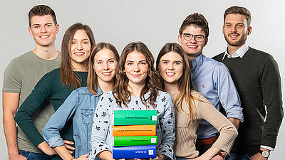 Studierende stehend nebeneinander und lächelnd mit Büchern