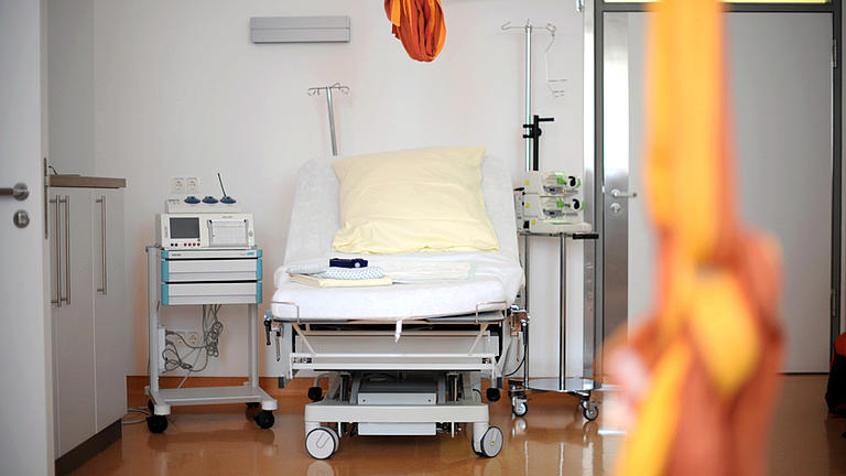 Blick in einen Kreißsaal, neben dem Entbindungsbett stehen verschiedene medizinische Geräte, von der Decke hängt ein Tuch.