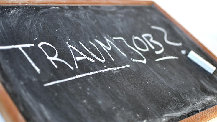 Auf einer schräg liegenden Schreibtafel mit Holzrand steht in Großbuchstaben das Wort "Traumjob"