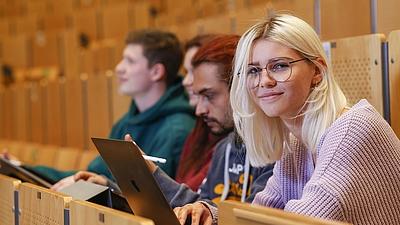 Zwei Studentinnen und zwei Studenten sitzen in einem Hörsaal und arbeiten mit Tablets und Laptops.