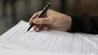 Männliche Hand schreibt mit einem Stift auf ein beschriebenes Blatt Papier