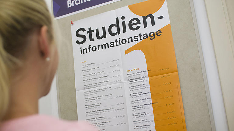 Eine junge Frau schaut sich ein Plakat zu einem Studieninformationstag an.