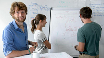 Drei Menschen stehen vor einen Flipchart und besprechen sich.