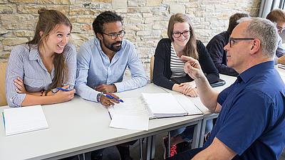 Ein Dozent erklärt einer Gruppe von Studierenden etwas.