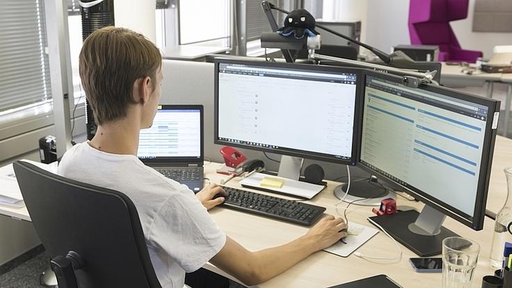Ein junger Mann arbeitet an einem Computer mit zwei Bildschirmen.