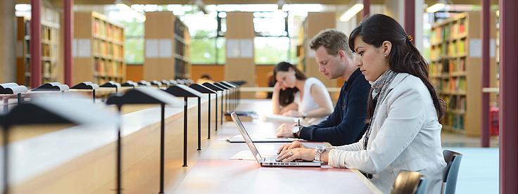 Studierende sitzen und lernen in einer Bibliothek.