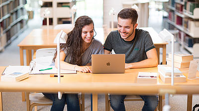 Zwei Studierende lernen gemeinsam in einer Bibliothek.