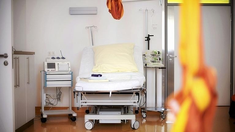 Blick in einen Kreißsaal. Neben dem Entbindungsbett stehen verschiedene medizinische Geräte. Von der Decke hängt ein Tuch.