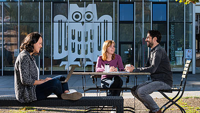 Studierende unterhalten sich vor dem Unigebäude im Sonnenschein