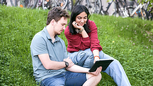 Eine Studentin und ein Student sitzen im grünen Gras mit Tablet.