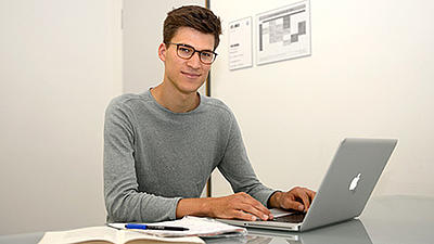 Ein junger Mann sitzt an einem Laptop.